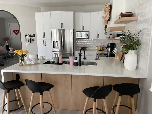 Bright kitchen with white flat-panel cabinets, a wood-tone peninsula with black bar stools and white quartz-look counters