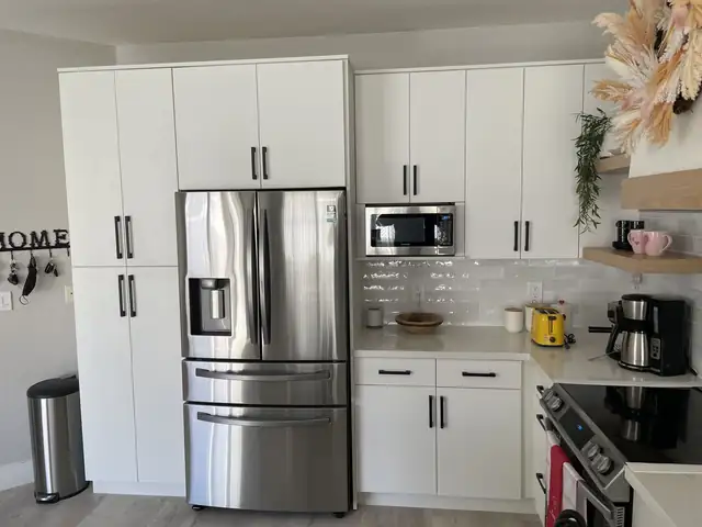 Wall of tall white flat-panel cabinets with black pulls around a stainless French-door refrigerator